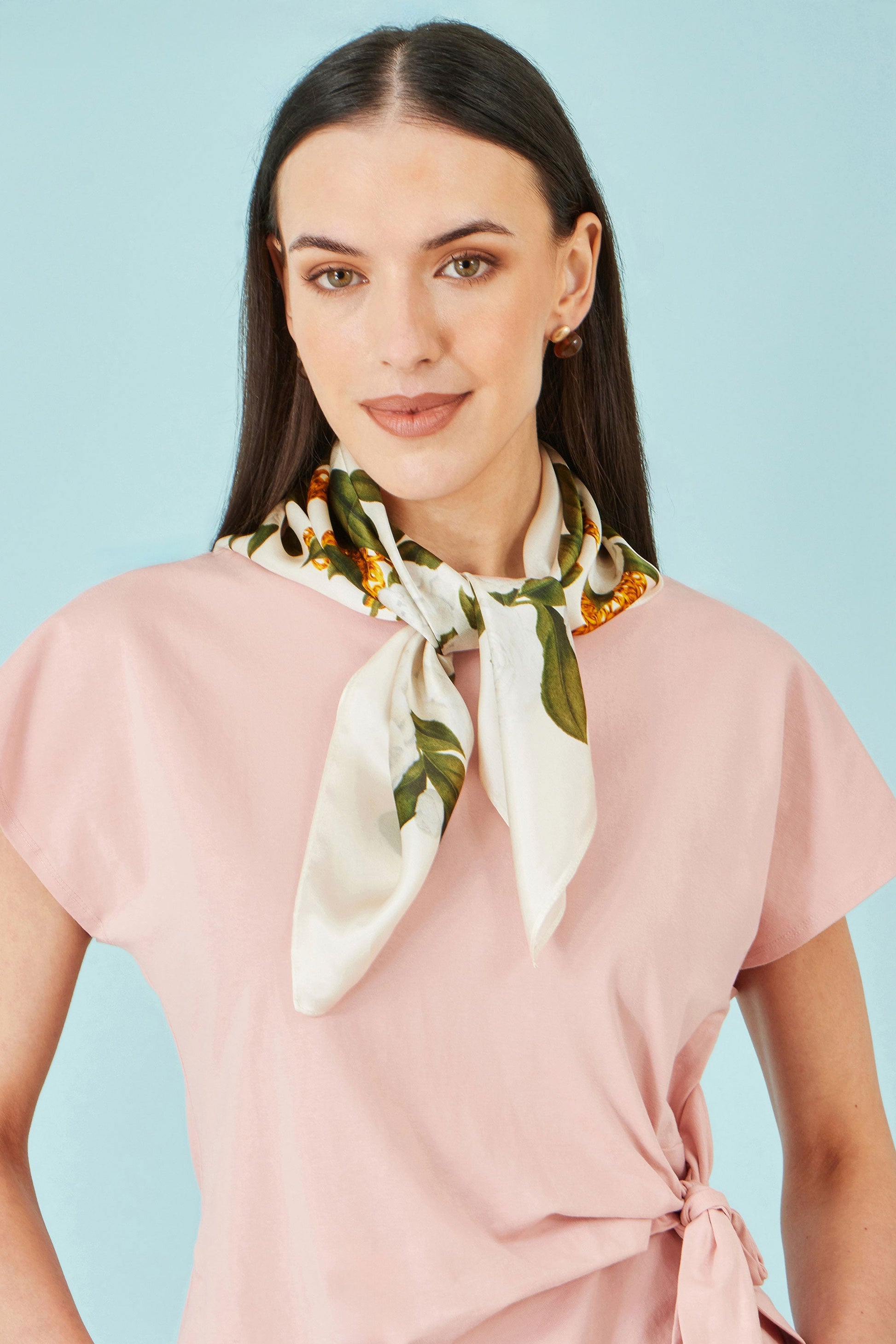 Woman wearing a pink top and a white scarf with green leaf patterns against a light blue background